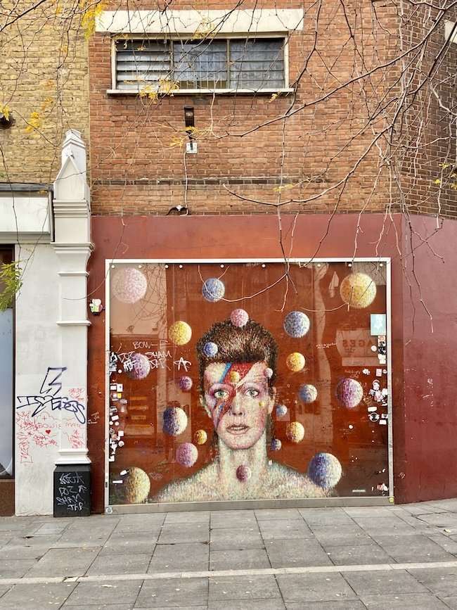 The iconic portrait mural of David Bowie painted on a brick wall in Brixton, serving as a vibrant tribute to the late musician.