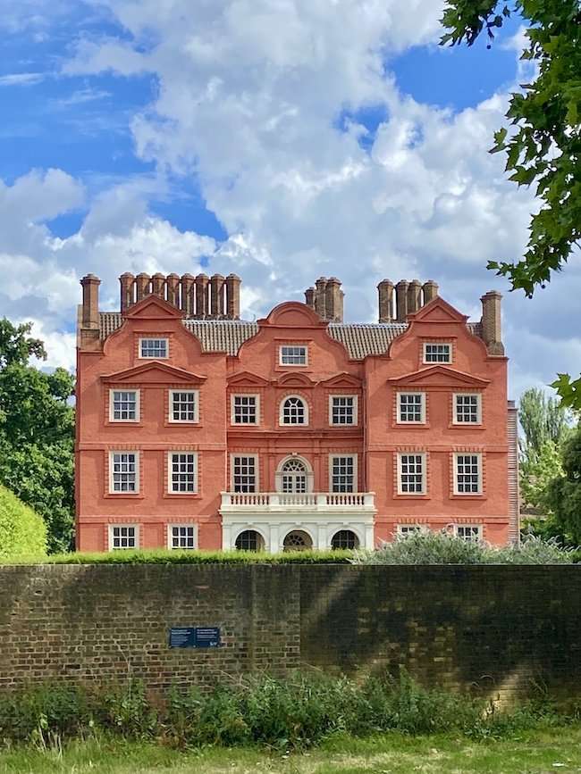 Flemish-bond red brick facade of historic Kew Palace nestled among trees within the botanical gardens.