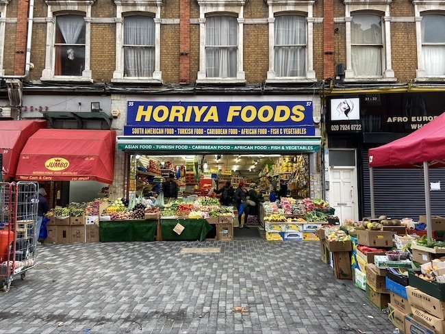 Lively pedestrian view of historic Electric Avenue in Brixton, featuring market stalls, vibrant storefronts, and multicultural crowds.