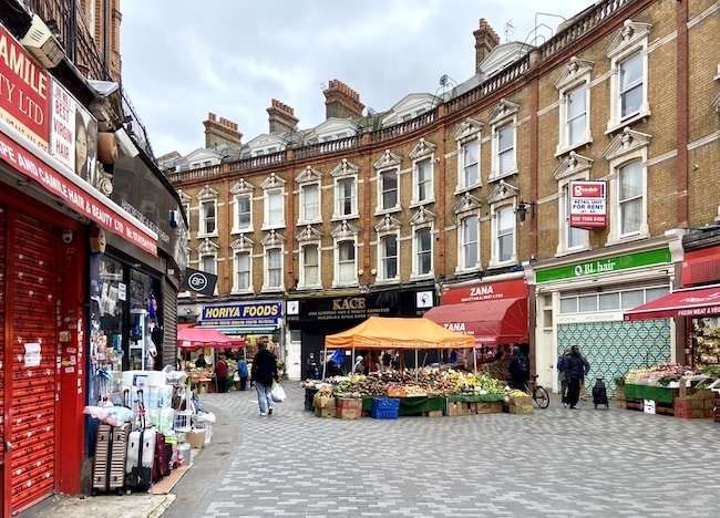Lively pedestrian view of historic Electric Avenue in Brixton, featuring market stalls, vibrant storefronts, and multicultural crowds.