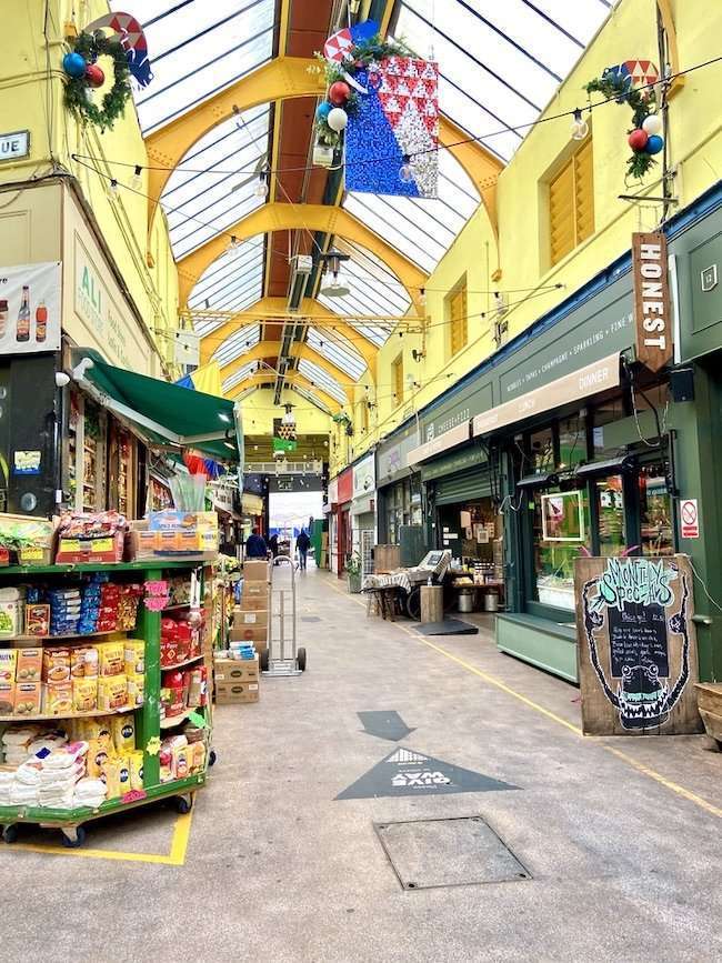 Bustling interior arcade of Brixton Village filled with independent food stalls, restaurants, and lively diners under a historic glass roof.