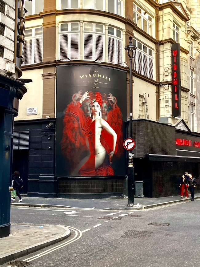 Historic exterior facade and glowing neon sign of The Windmill venue in Soho, London.