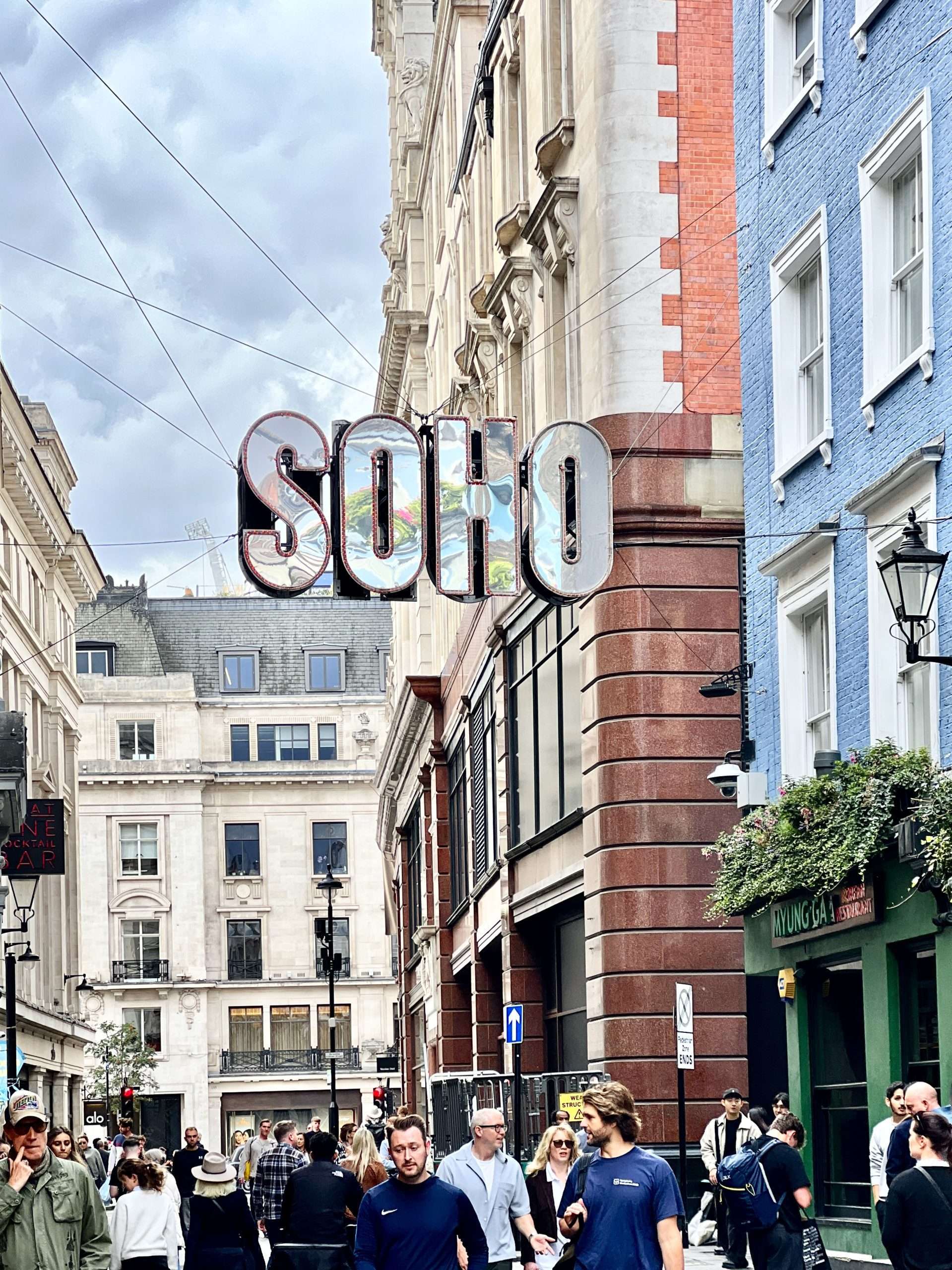 Crowd of pedestrians walking through the lively shopping streets of Soho, London on a sunny afternoon.