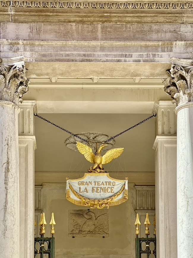 Primo piano simmetrico dell'insegna dorata e dei dettagli architettonici del Gran Teatro La Fenice a Venezia, fotografia di Alessandra Cervetti selezionata per il sito ufficiale di Accidentally Wes Anderson.